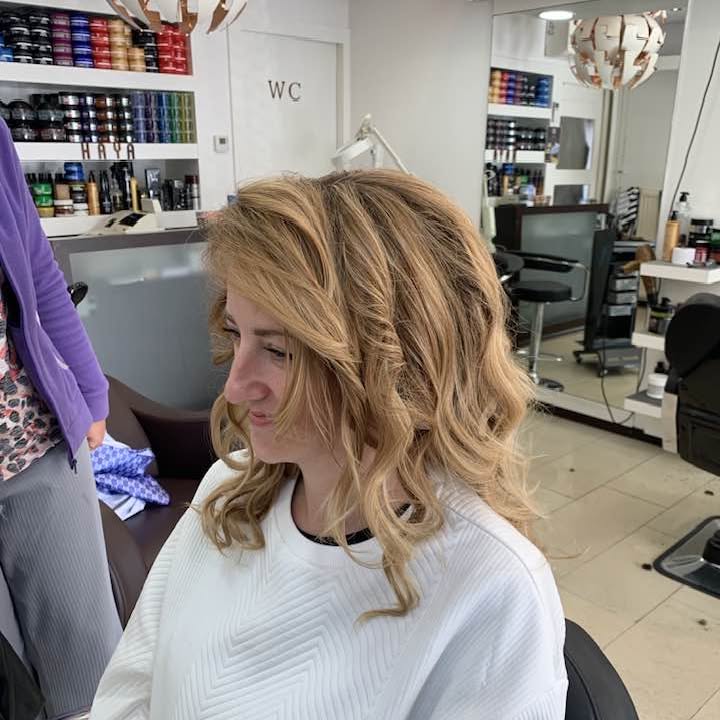 Klant met halflang blond haar in golven, lachend in de stoel